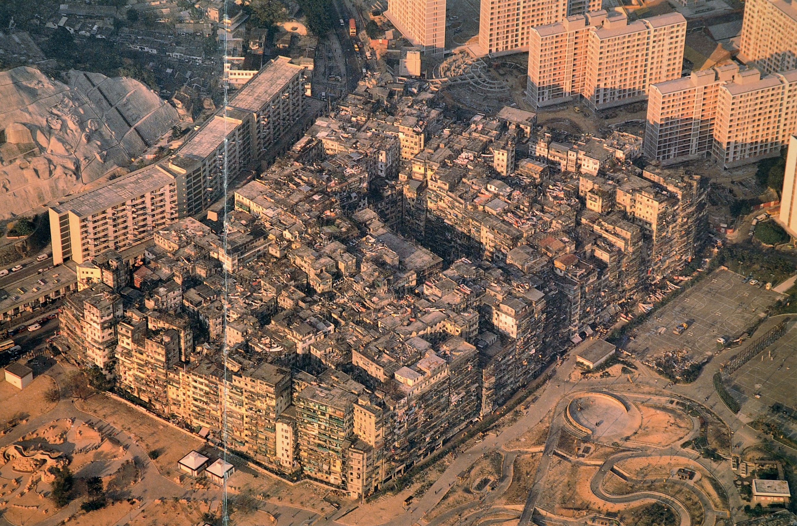 Seemingly a single organic block, the 350 or so buildings of the Kowloon Walled City appeared as a rough parallelogram when seen from the air. Enclosing 2.7 hectares - or nearly 7 acres — the perimeter of the City followed the line of the old fort's former wall. As this could no longer be accurately pinpointed, the City had undoubtedly grown or receded in places. Taken in 1989, this aerial view shows the new park laid out on the site of the Sai Tau Tsuen squatter settlement which once mushroomed from the southern and western edges of the City.